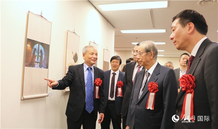 “湖州印象”攝影展主創(chuàng)、世界華人攝影協(xié)會副會長馮學(xué)敏向吳江浩大使、福田康夫前首相等嘉賓介紹展出作品。（人民網(wǎng) 許可攝）