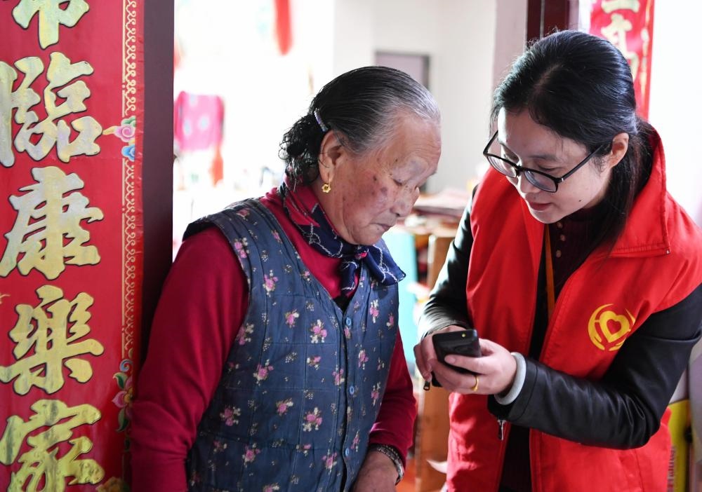 在福州市長樂區(qū)航城街道籌岐村，智慧養(yǎng)老平臺派駐社區(qū)的助老員（右）在為老人陳鳳英（左）講解養(yǎng)老定制手機的用法（2021年11月26日攝）。新華社記者 魏培全 攝