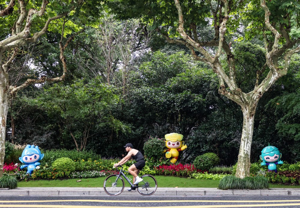 市民在杭州市南山路上一處亞運會主題吉祥物雕塑前騎自行車。