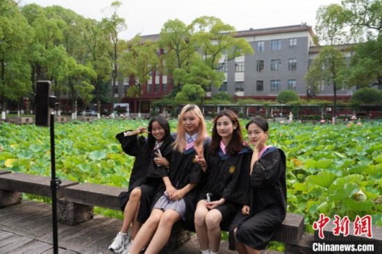 6月19日，時(shí)值一年畢業(yè)季，四川大學(xué)望江校區(qū)荷花池里的荷花盛開，成為了畢業(yè)生們的打卡圣地，吸引了眾多畢業(yè)生拍照留念。圖為畢業(yè)生在荷花池邊拍照留念。中新社記者 安源 攝