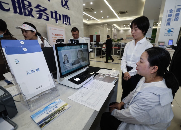 在浙江省嘉興市秀洲區(qū)王江涇鎮(zhèn)便民服務(wù)中心的“跨域通辦·云綜窗”窗口，辦理開業(yè)登記的個(gè)體工商戶（右一）通過該系統(tǒng)與江蘇省蘇州市吳江區(qū)盛澤鎮(zhèn)行政審批局工作人員視頻連線，進(jìn)行身份讀取及材料線上審核（2024年5月9日攝）。新華社記者 徐昱 攝